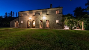 A large stone building with multiple arched doorways and windows, illuminated by exterior lighting.