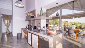 A modern kitchen with a large island, built-in appliances, and a dining area with outdoor seating. - Villa Aura 6 in Giardini Naxos (Giardini Naxos)
