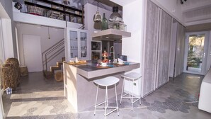 A modern kitchen with a central island, white bar stools, and a staircase leading to an upper level. - Villa Aura 6 in Giardini Naxos (Giardini Naxos)