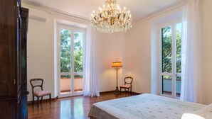 A spacious bedroom with a large bed, two chairs, a floor lamp, and a chandelier. - Villa Dell Angelo 10 (Rosignano Marittimo)