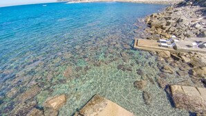 A rocky shoreline with clear water, a small pier, and a building in the background. - Villa Dell Angelo 10 (Rosignano Marittimo)