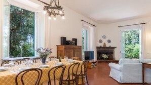 A dining area with a table set for six, a fireplace, and a sofa in a room with large windows. - Villa Dell Angelo 10 (Rosignano Marittimo)