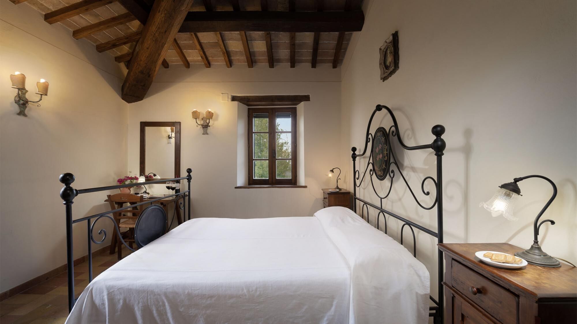 Un dormitori amb llit, escriptori, cadira, prestatge i finestra, a més d'aparells de paret.