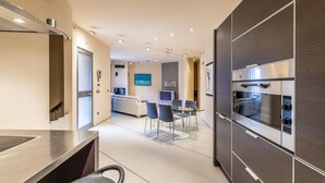 Una cocina moderna con horno integrado y comedor con mesa y sillas de vidrio.