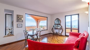 A spacious living room with a red sofa, a dining table with chairs, a large window with a view, and a mirror on the wall. - Villa Elda 6 in Loano (Loano)