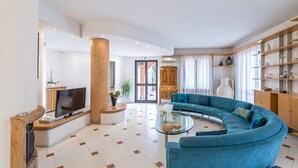 Una sala de estar moderna con un sofá azul curvo, una mesa de centro de vidrio y un televisor.