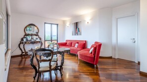 A living room with a wooden parquet floor, a red sofa, a dining table with chairs, a mirror, and a painting on the wall. - Villa Elda 6 in Loano (Loano)