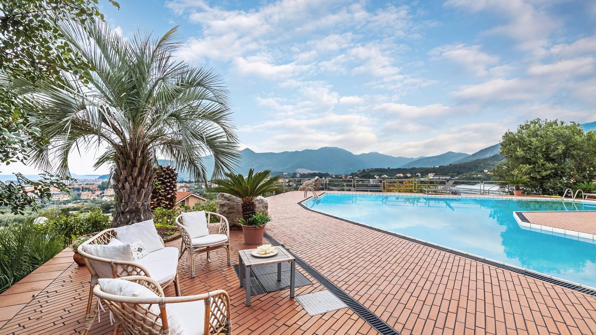 Area piscina con sedie in vimini, un tavolo e vista sulle montagne.