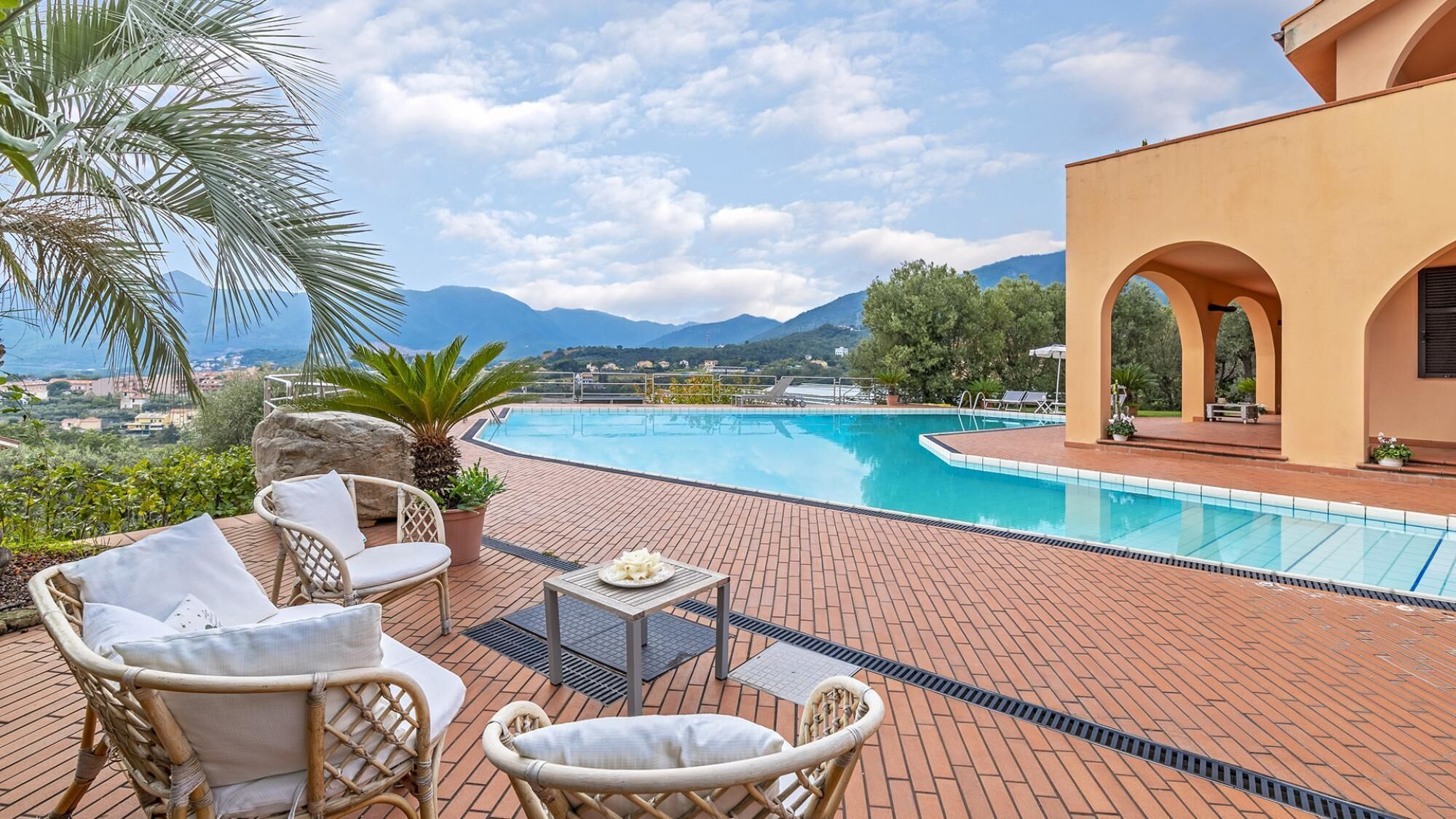 Area piscina con sedie in vimini, un tavolo e vista sulle montagne e sulla piscina.
