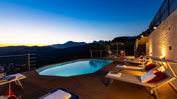 A poolside area with lounge chairs and a view of mountains at dusk. - Villa Elena 9 1 in Coli (Massarosa)