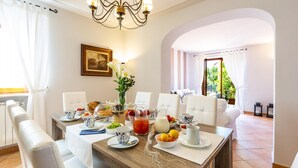 A breakfast setting with a wooden table, white chairs, and a chandelier. - Villa Elena 9 1 in Coli (Massarosa)