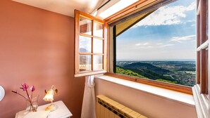A bathroom with a large window offering a scenic view of a valley and distant cityscape. - Villa Elena 9 1 in Coli (Massarosa)