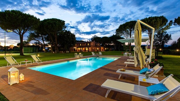 Une piscine entourée de chaises longues et agrémentée d’une pergola, le tout niché au milieu des arbres, avec un bâtiment visible au loin.