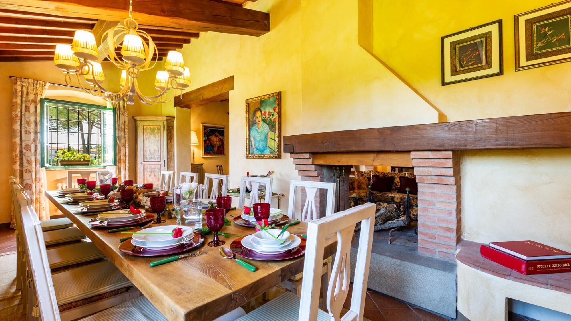 Un comedor con una larga mesa de madera dispuesta para una comida, una chimenea y una araña.