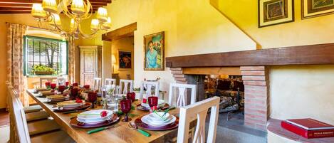 Un comedor con una larga mesa de madera dispuesta para una comida, una chimenea y una araña.
