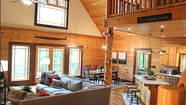 Interior de una cabaña con sala de estar, comedor, cocina y un dormitorio en lo alto.