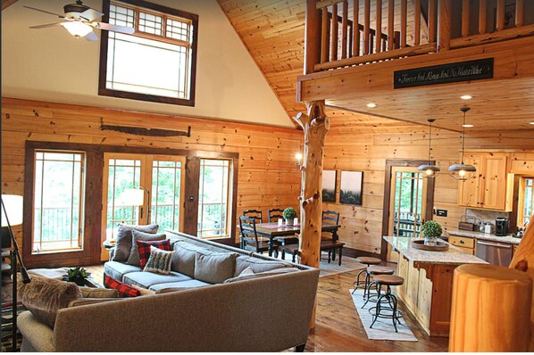 A cabin interior with a living room, dining area, kitchen, and a loft bedroom.