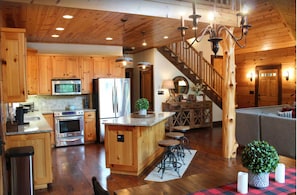 A spacious kitchen with wooden cabinets, stainless steel appliances, a central island with stools, and a staircase leading to a loft area.