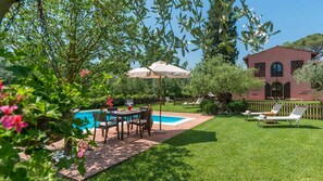 Un jardin avec une piscine, une table à manger avec des chaises et un coin salon avec des transats.