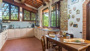 A rustic kitchen with wooden beams, a stone wall, and a tiled backsplash.