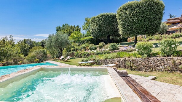 Piscina com deck de pedra, rodeada por vegetação exuberante e um muro de pedra.