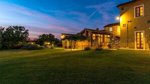 A well-lit, two-story house with a stone facade, a covered patio, and a neatly maintained lawn.