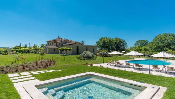 A pool area with a hot tub, lounge chairs, and umbrellas.