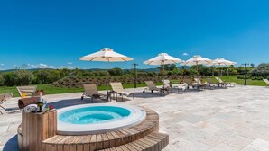 A hot tub surrounded by lounge chairs and umbrellas, with a view of a landscaped garden and hills in the background.