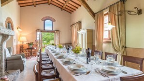 A long dining table set for a meal with chairs, a stone pillar, and a view of the outdoors.