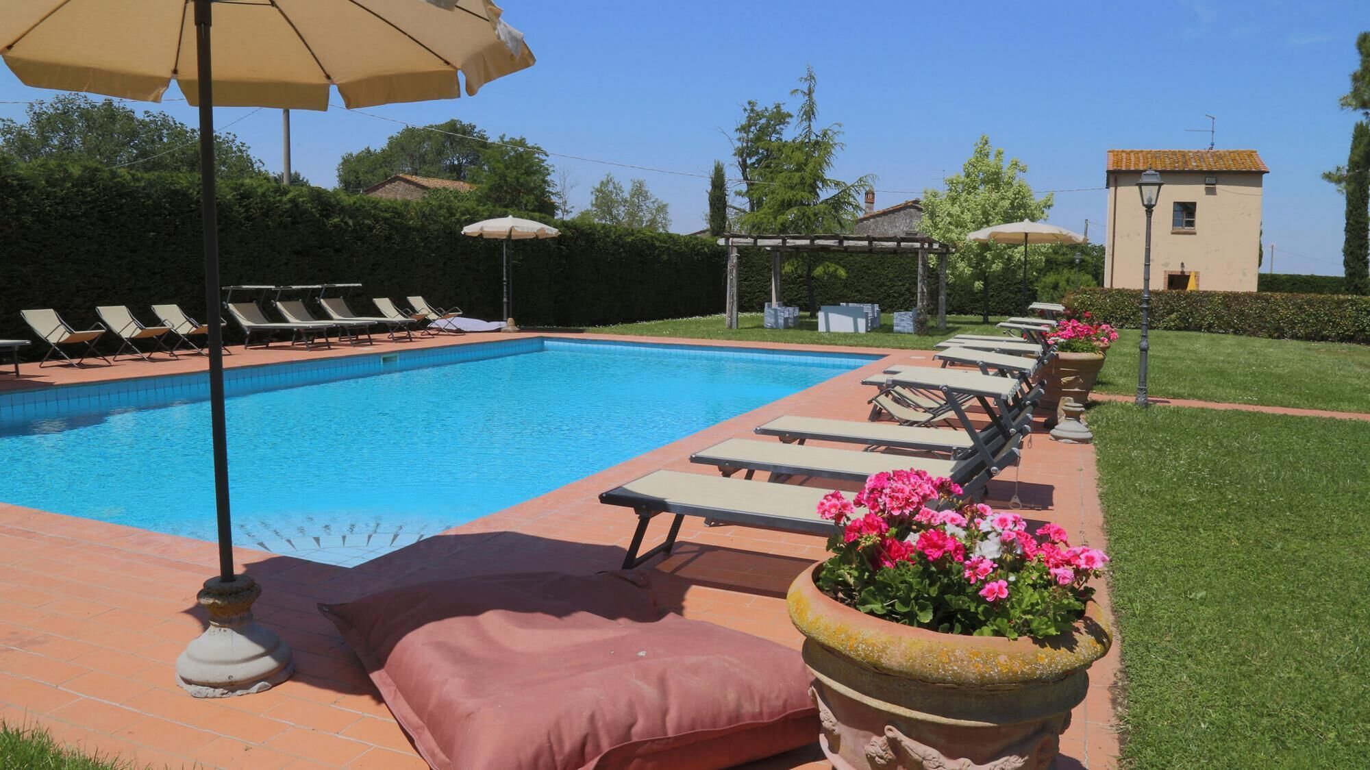 Une piscine entourée de chaises longues et de parasols, avec une pelouse bien entretenue et un bâtiment visible au loin.