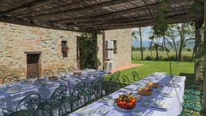 Een buitenrestaurant met een stenen muur, een overdekte pergola en uitzicht op het landschap.