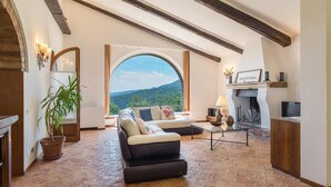 Un salon chaleureux avec une grande fenêtre en arc de cercle, une cheminée et un coin salon confortable.