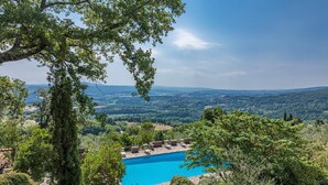 Un espace piscine doté de chaises longues, entouré d’arbres et offrant une vue sur un paysage pittoresque.