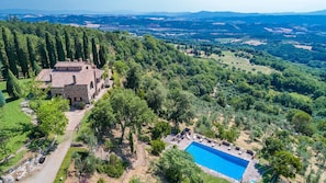 Uma grande moradia de pedra com piscina, rodeada por vegetação exuberante e uma vista panorâmica de colinas ondulantes.