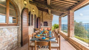 A covered outdoor dining area with a brick wall, wooden beams, and a view of the landscape. - L Alcova 8 2 in Sarteano (Sarteano)