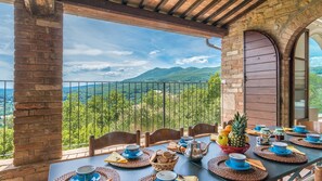 Terraço com mesa posta para o pequeno-almoço, com vista para uma paisagem montanhosa.