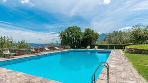 Ein rechteckiger Pool mit einer Metallleiter, umgeben von Steinfliesen und ausgestattet mit mehreren Liegestühlen.