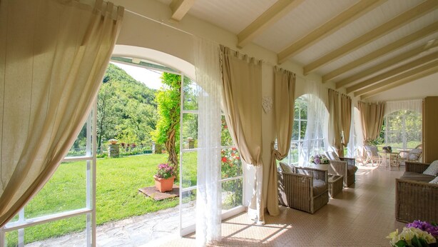 Una habitación amplia con ventanas grandes, mobiliario de mimbre y vistas a un jardín exuberante.