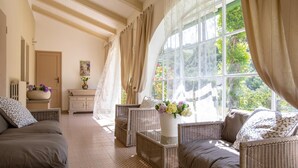 Una habitación soleada con muebles de mimbre, un ventanal con cortinas y un jarrón con flores.