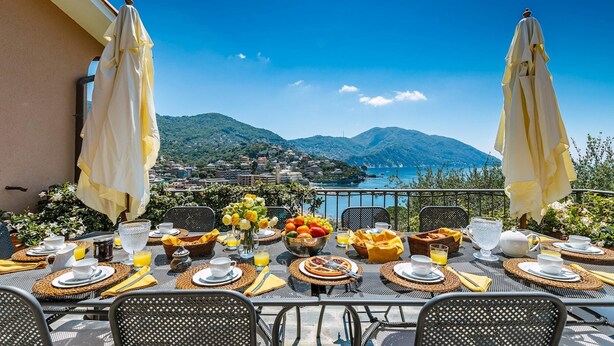Una mesa lista para el desayuno, con una vista panorámica de un pueblo costero y montañas.