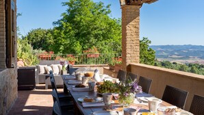 An outdoor dining area with a view of the countryside, wicker furniture, and a table set with food and drinks. - La Vecchia Fonte 15 (Volterra)