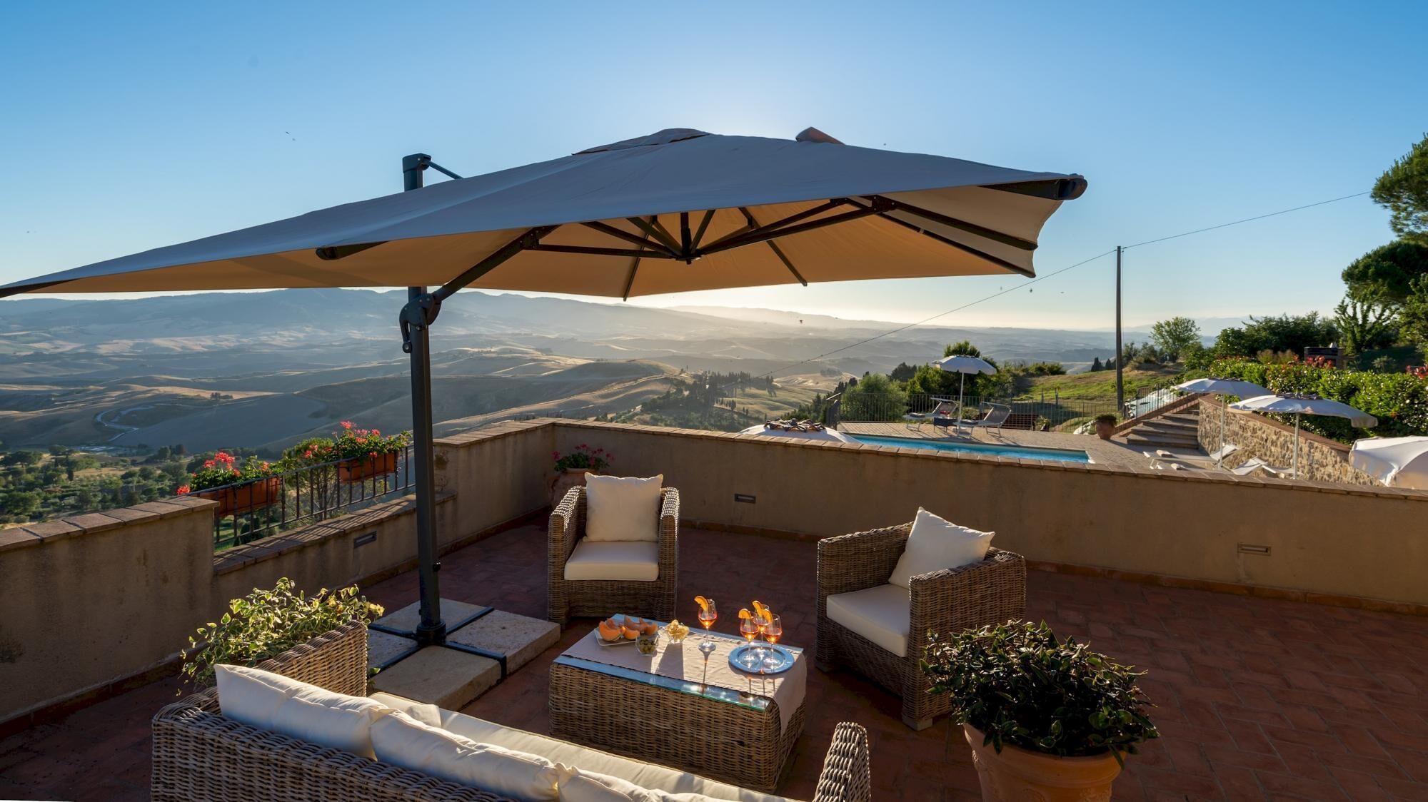 A terrace with wicker furniture, a table with drinks, and a view of rolling hills.