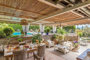 An outdoor patio with wicker furniture, a pool, and potted plants.
