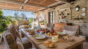 An outdoor dining area with a stone wall, wicker furniture, and a variety of fruits and pastries on the table. - La Capannina 2 2 in Camucia (Cortona)
