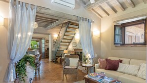 A cozy living room with a staircase, a sofa, a coffee table, and a dining area with chairs and a table. - La Capannina 2 2 in Camucia (Cortona)