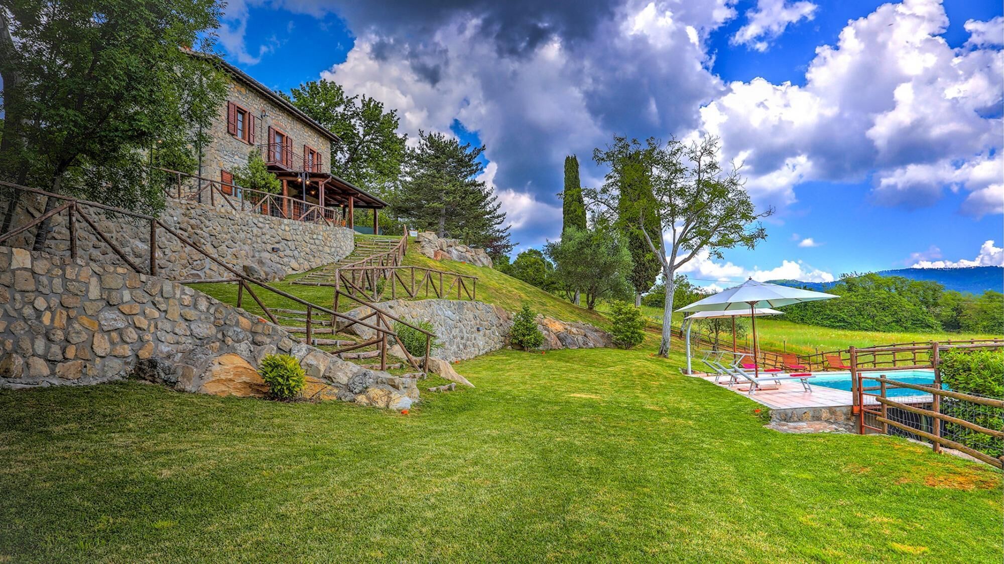 A stone staircase leading to a stone building with a pool area and outdoor seating.