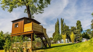 A wooden treehouse with a balcony, surrounded by tall trees and a grassy area. - La Casa Di Nan 8 in Forli (Forlì)