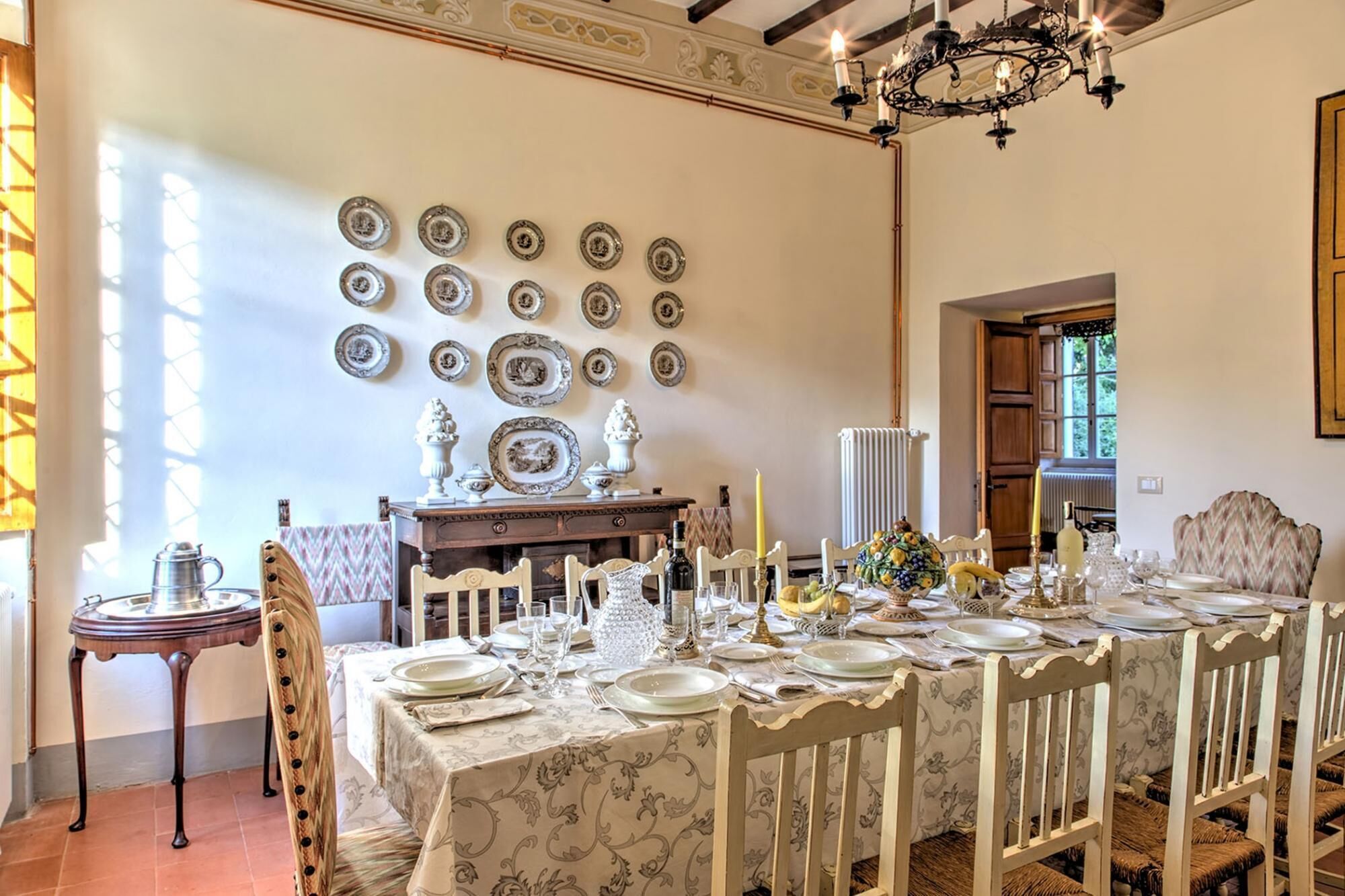 Uma sala de jantar com uma mesa longa posta para refeição, rodeada de cadeiras.