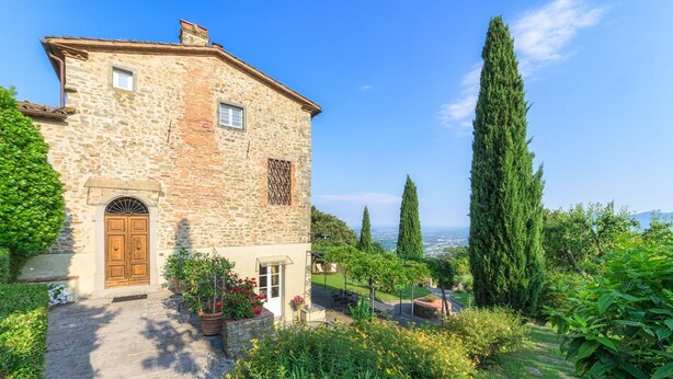 A stone building with a wooden door, potted plants, and a view of the landscape. - Villa Primo Sole 22 (Lucca)