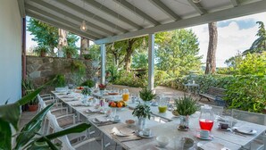 An outdoor dining area with tables set for a meal, surrounded by greenery and a stone wall. - Villa Leonardo 30 6 (Figline e Incisa Valdarno)